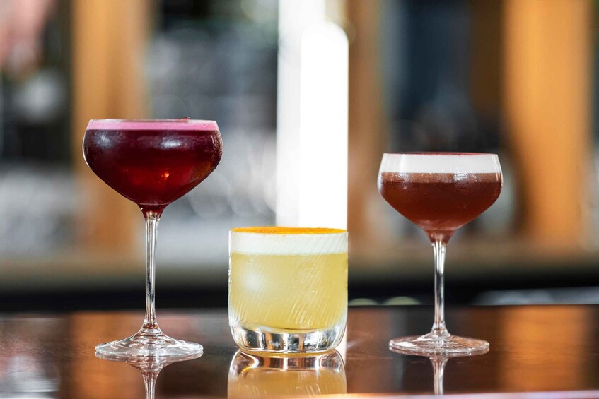 Three different cocktails in stemmed glasses on a reflective surface. 4