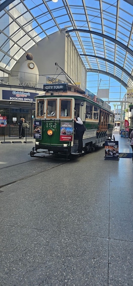 A green tram with the number 152 at a station with a glass roof and a 'City Tour' sign. 1