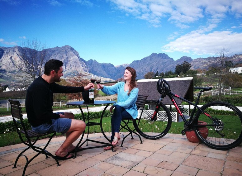 Two people toasting with wine glasses, a bicycle, and a scenic mountain backdrop. 2