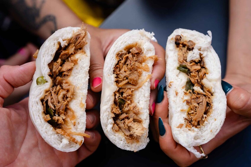 Three hands holding a burrito with shredded meat and vegetables. 5