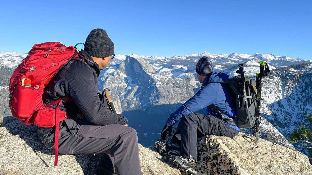 Two hikers on a mountain peak with snow-covered mountains in the background. 4