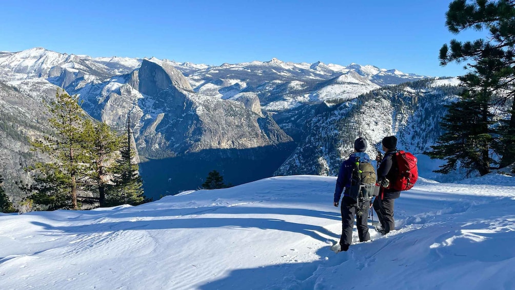 Two people hiking on a snow-covered mountain with a clear view of a prominent mountain peak in the background. 5