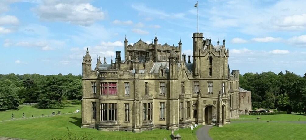 A large, historic stone building with multiple towers and a well-maintained lawn. 4