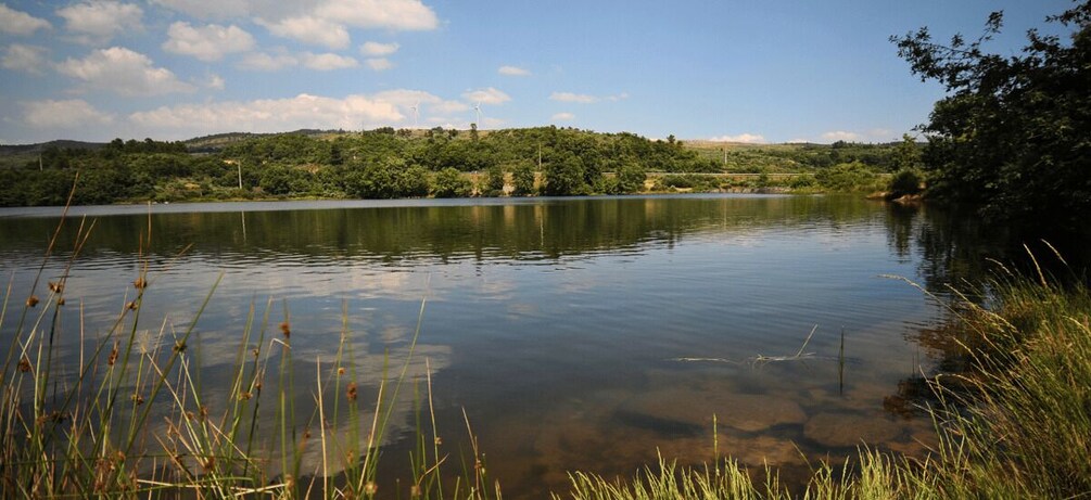 A calm lake with clear water, surrounded by lush greenery and hills. 5