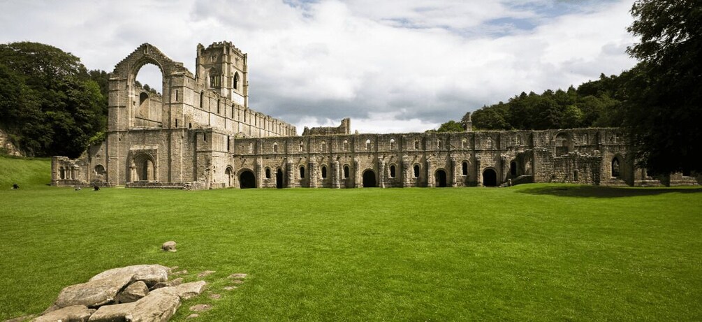 A historic stone building with arches and ruins, surrounded by a well-maintained lawn. 2