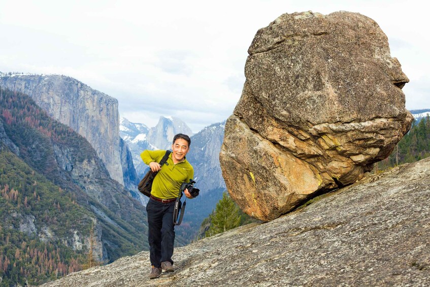 A person hiking with a camera, a large rock formation, and a mountainous landscape. 4