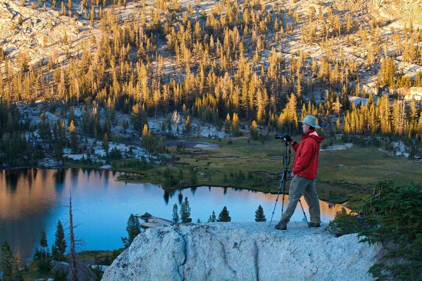 A person with a camera on a tripod overlooking a lake surrounded by forested mountains. 2