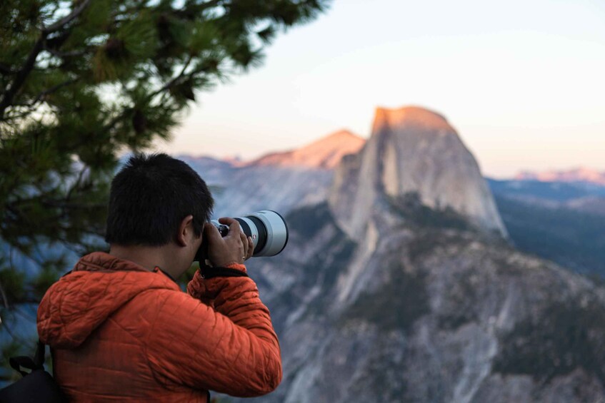 A person in an orange jacket taking a photograph of a mountain peak. 5