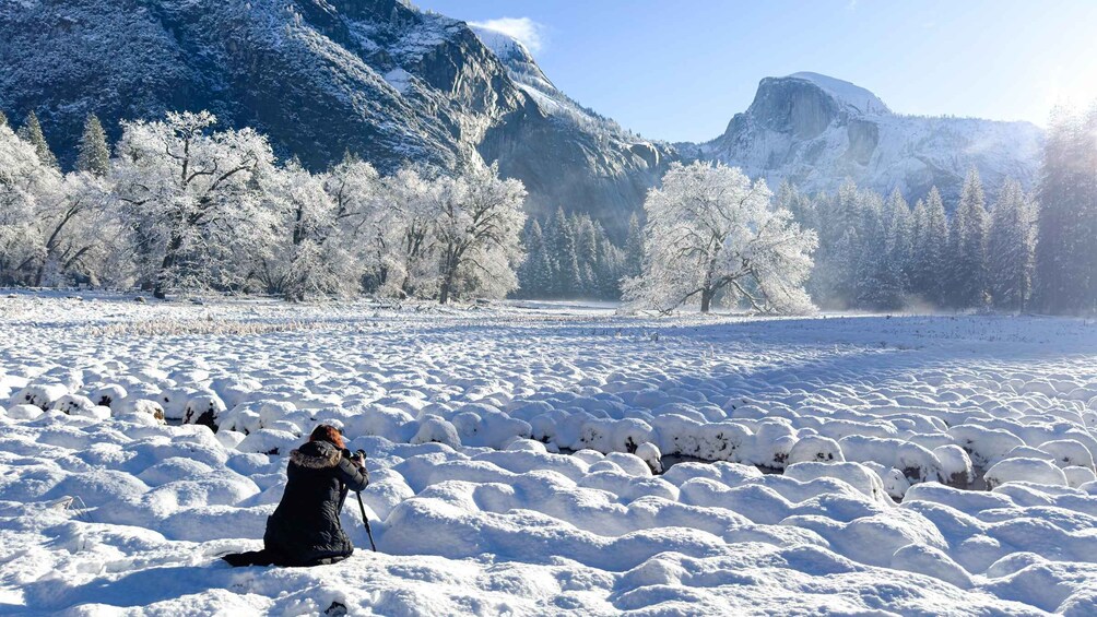 A person taking a photo in a snowy field with mountains in the background. 3