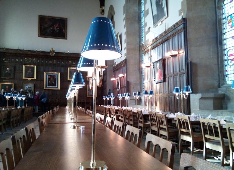 A long wooden table with chairs, blue lamps, and framed pictures on the walls. 1