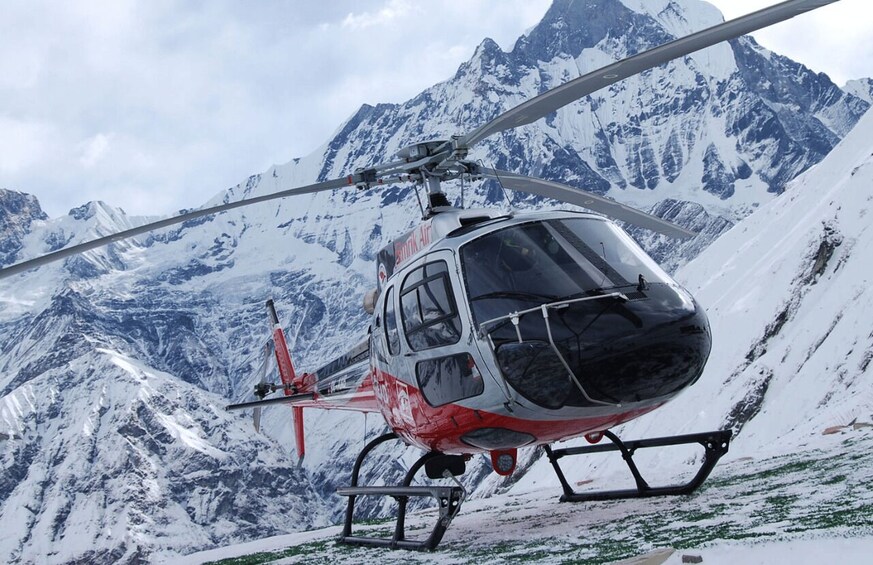 A red and black helicopter parked on a snowy mountain with snow-covered peaks in the background. 5