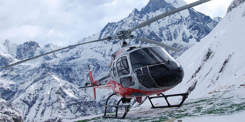 A helicopter with a red and black color scheme parked on a snowy mountain slope. 1