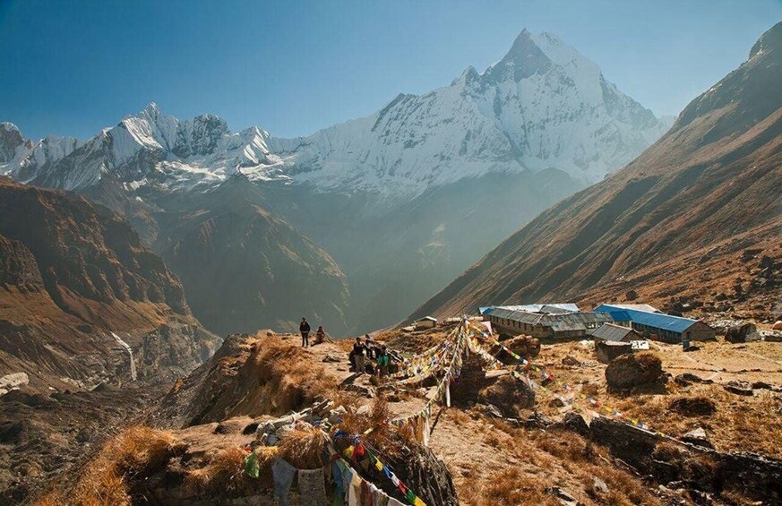 A mountainous landscape with a prominent peak, a trail with trekkers, and a small settlement with buildings. 3
