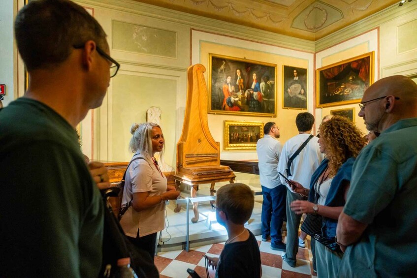 A museum interior with visitors observing a large harpsichord and paintings on the walls. 3