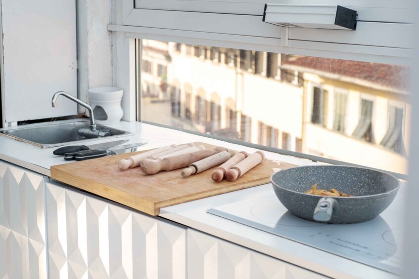 Een keuken met een snijplank, deegrollers, een koekenpan en een raam met uitzicht op gebouwen. 5