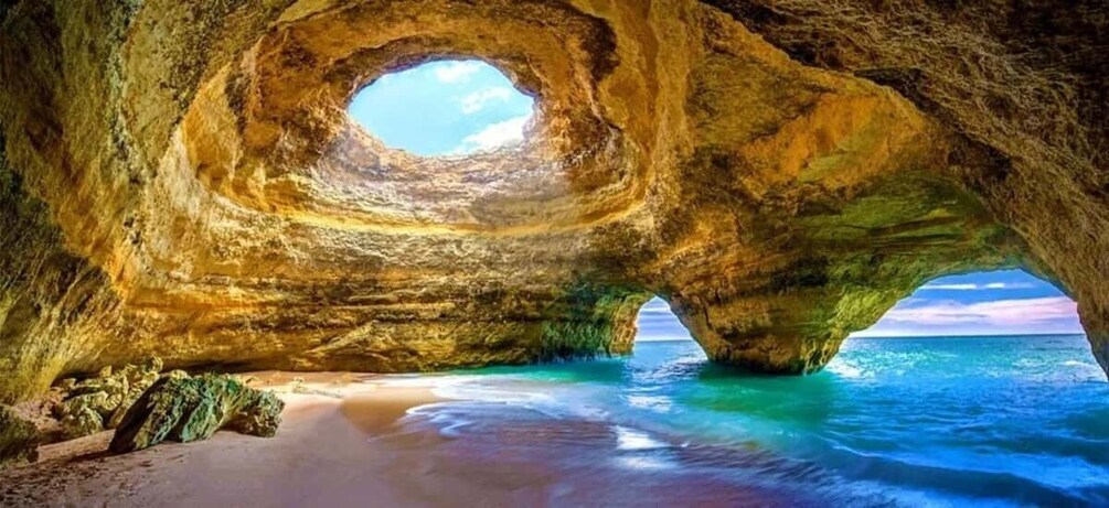 A natural rock formation with a circular opening, a beach, and the ocean. 1