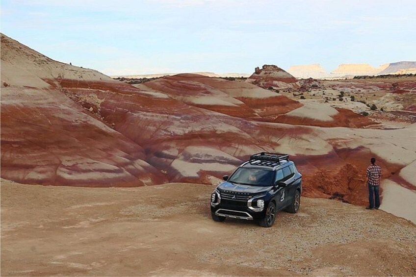 A black SUV parked on a dirt road in a desert landscape with red and beige terrain. 3