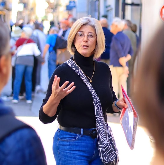 A person walking on a busy street, gesturing with one hand, holding a pink folder. 3