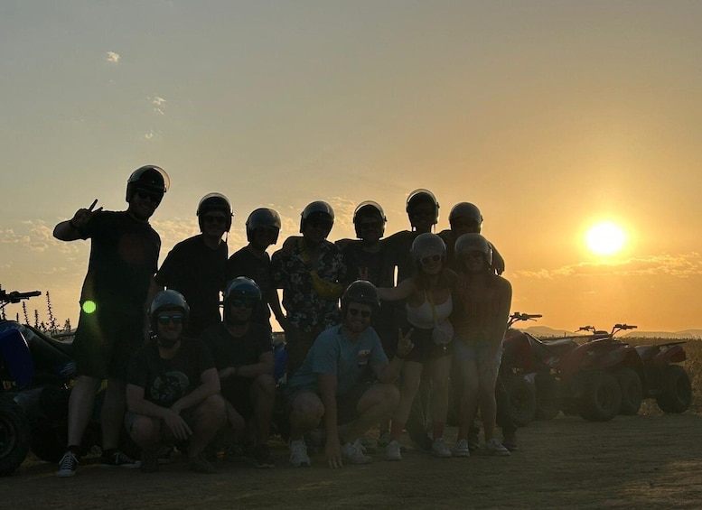 A group of people with helmets posing for a photo at sunset with vehicles in the background. 3