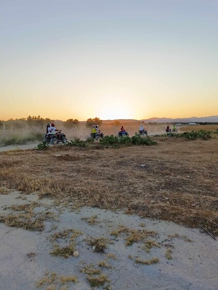 A group of people riding ATVs on a dirt path during sunset. 4