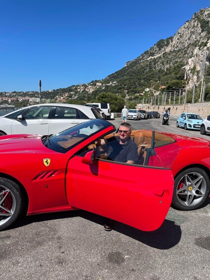 A red Ferrari convertible parked on a coastal road with a mountainous backdrop. 3