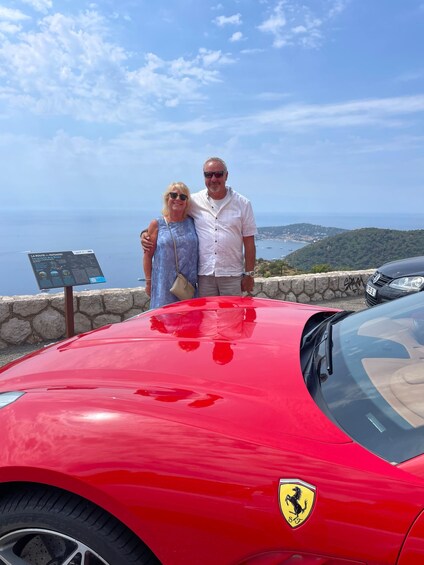 A red Ferrari parked near a stone wall with a scenic coastal view in the background. 4