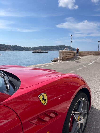 A red Ferrari parked by a waterfront with a clear sky. 1