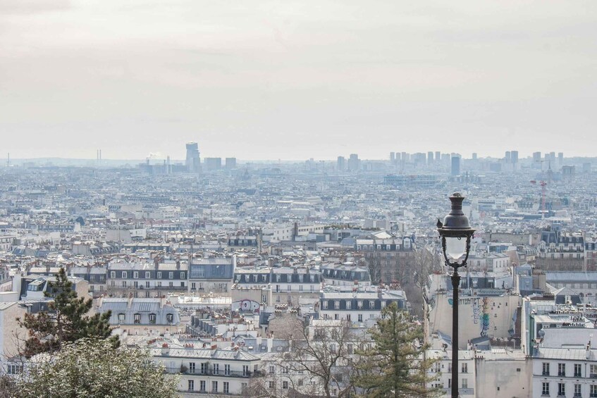 A cityscape with dense urban buildings, a prominent street lamp, and distant high-rise structures. 1