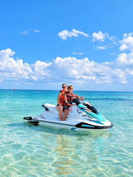 Two people on a jet ski in clear turquoise water with a bright blue sky and scattered clouds. 1