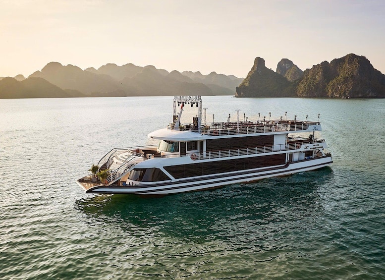 A large, multi-deck boat on calm water with a mountainous backdrop. 5