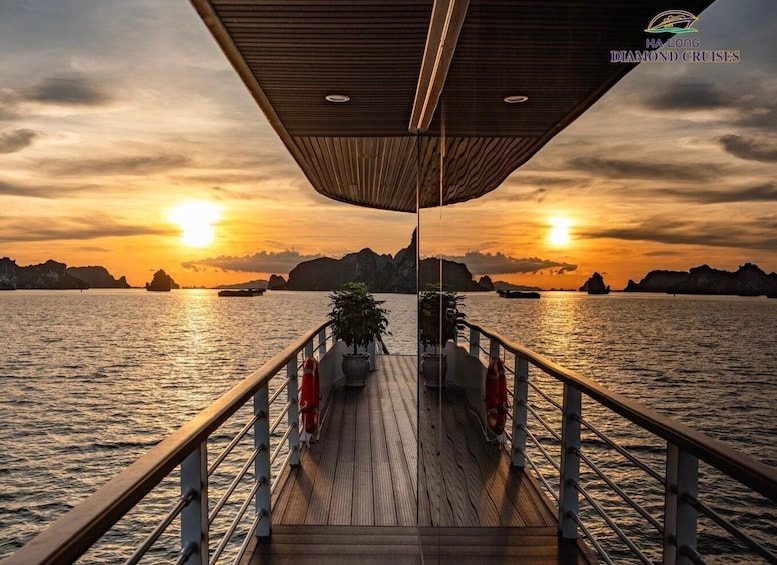 A wooden deck with railings, potted plants, and a sunset over water with boats and rocky formations in the distance. 3