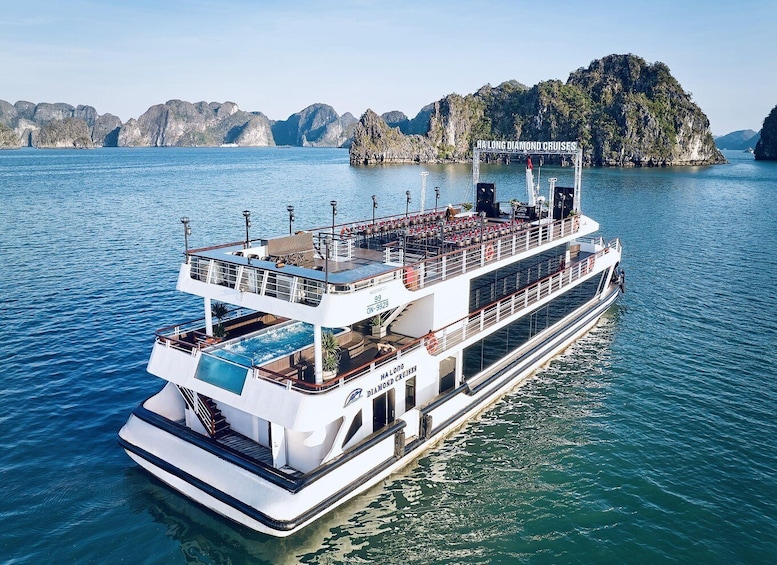 A large white cruise ship with a swimming pool and a deck area, sailing near a rocky island. 1
