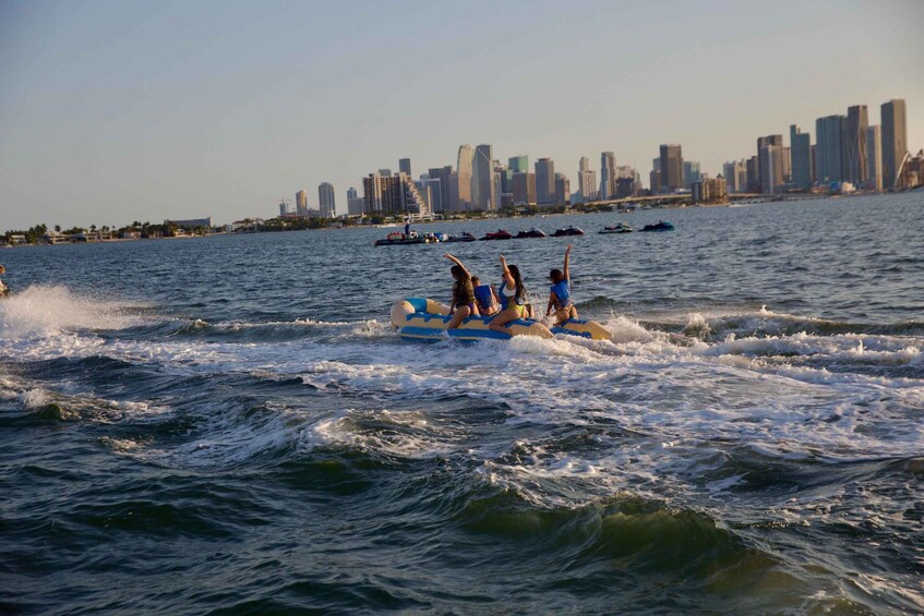People on a watercraft in a body of water with a city skyline in the background. 4