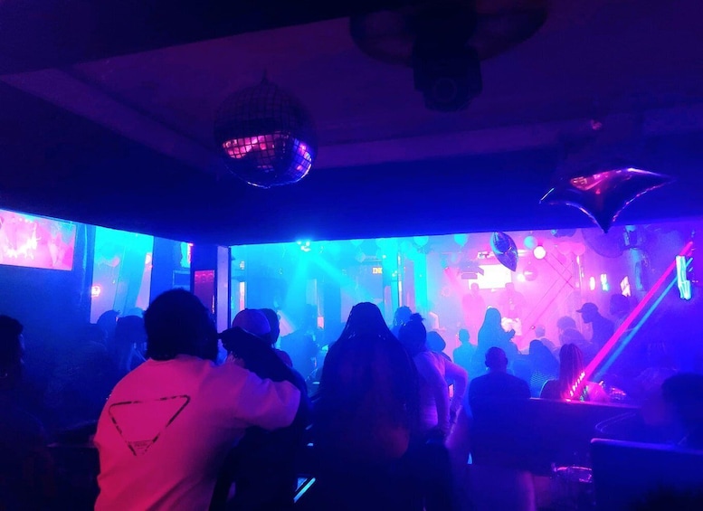 A crowded indoor venue with people dancing, disco lights, and a DJ booth. 2