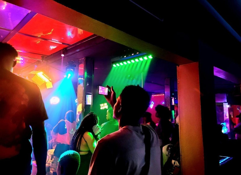 A crowded indoor space with colorful lighting and a DJ booth. 1