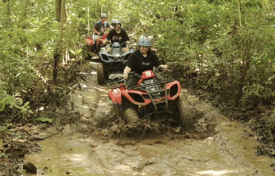 A group of people riding ATVs on a muddy trail in a forest. 1
