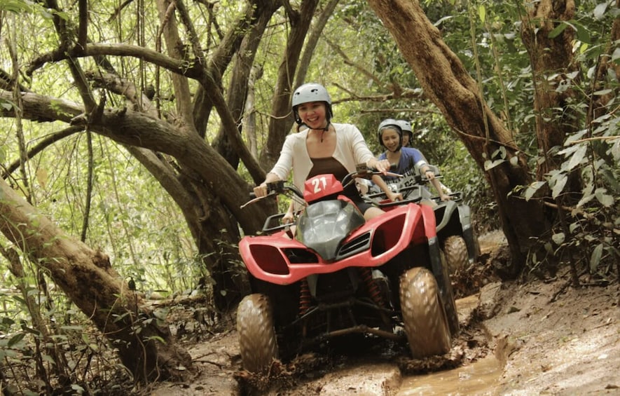 Two people riding a red ATV through a forested area with muddy terrain and trees. 5