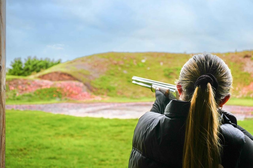 A person aiming a shotgun at a target in an outdoor setting. 4