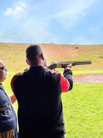 A person aiming a shotgun at a target in an outdoor range. 2