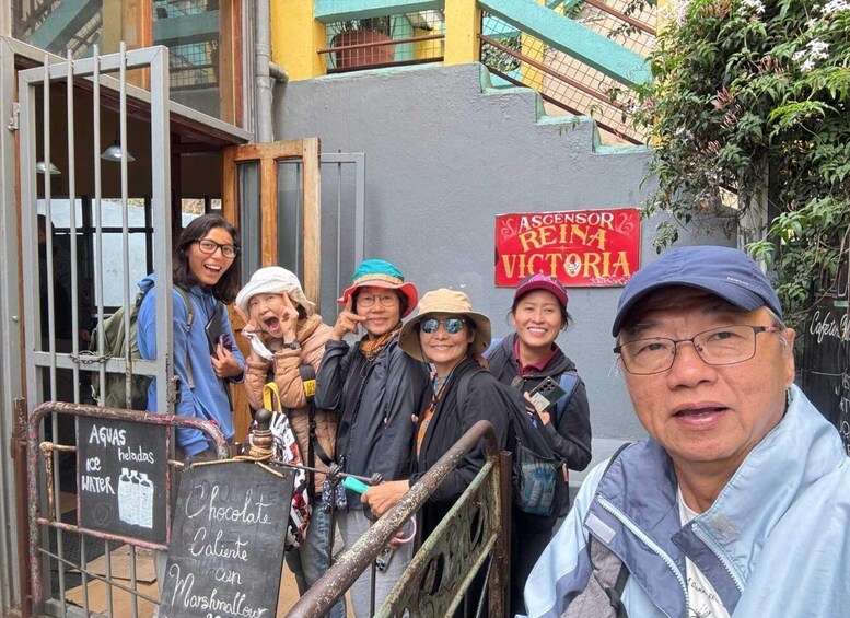 A group of people outside a café named 'Ascensor Reina Victoria,' with a sign offering chocolate, ice cream, and marshmallows. 1