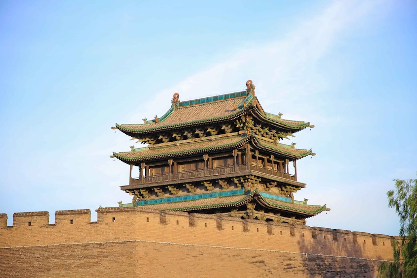A traditional multi-tiered pagoda with ornate eaves and a brick wall in the foreground. 1