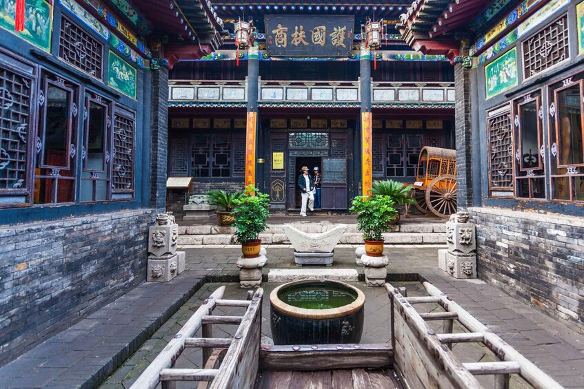 A traditional Chinese courtyard with ornate architecture, a central water feature, and a couple standing in the entrance. 4