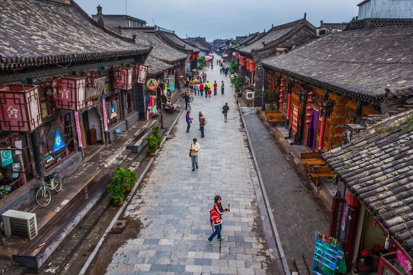 A narrow street lined with traditional buildings, a person walking, and a bicycle parked on the side. 3