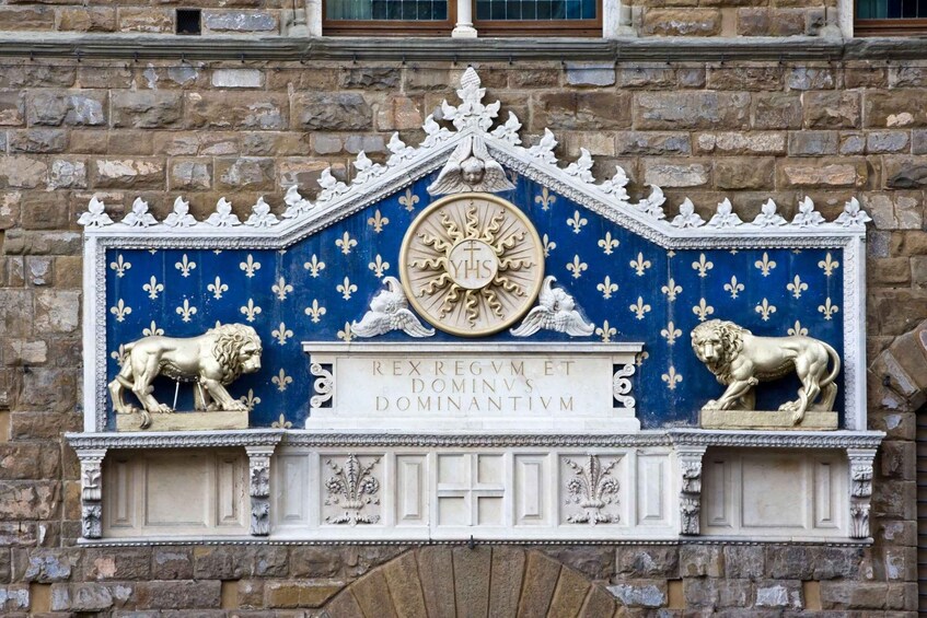 A stone wall with a blue and gold emblem featuring a sun, two lions, and Latin inscriptions. 5