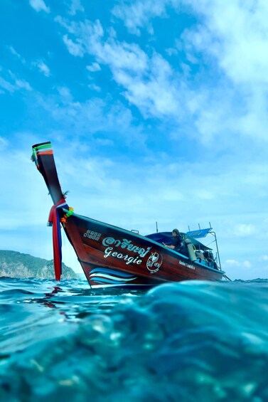 A boat with a long wooden tail and a red ribbon, sailing on clear blue water. 3