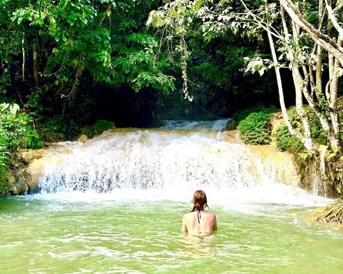 Une personne se trouve dans une étendue d’eau naturelle, entourée d’une végétation luxuriante et d’une cascade. 4