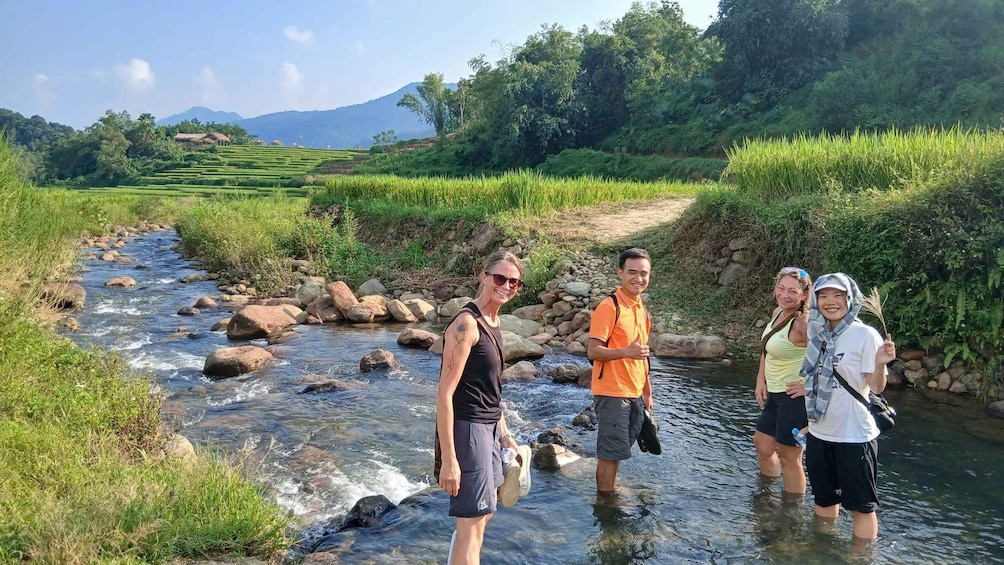 Un groupe de personnes se tient dans une rivière, entouré d’une végétation luxuriante et de champs en terrasses. 2