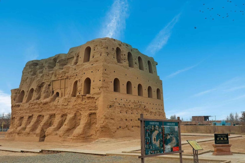 A large, ancient, multi-tiered structure with arched windows, surrounded by a paved area with informational signs. 3