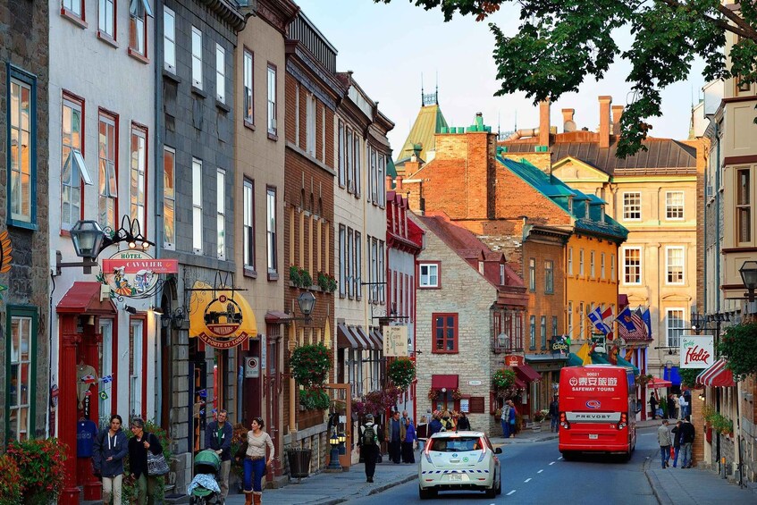 A street lined with historic buildings, a red bus, and pedestrians. 4
