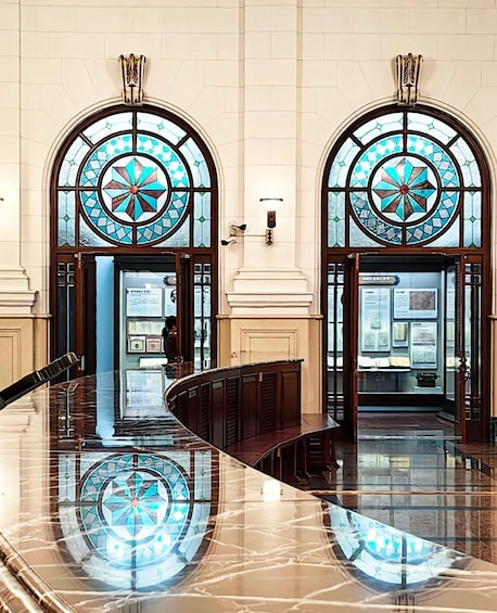 A lobby with two large arched stained glass windows and a polished marble floor. 4